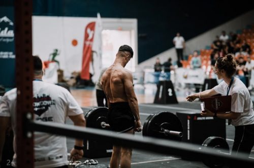 A weightlifting athlete prepares for a lift during a competition with judges observing.